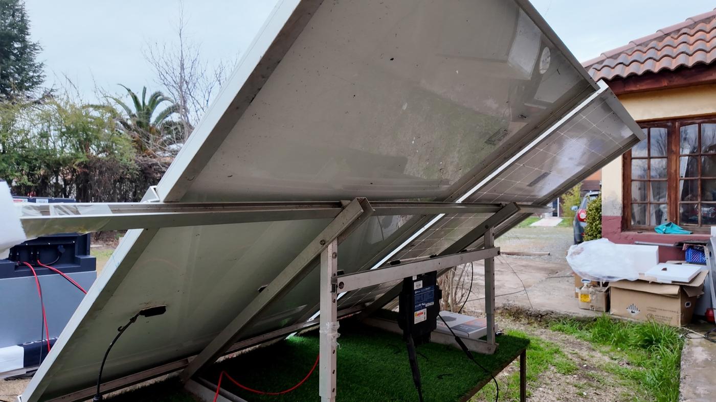 Paneles solares sobre una estructura en el suelo, junto a una casa